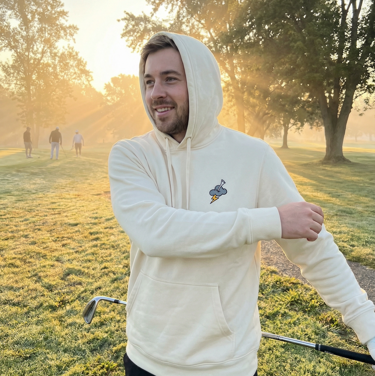 Man in a white hoodie standing on a golf course with trees in the background