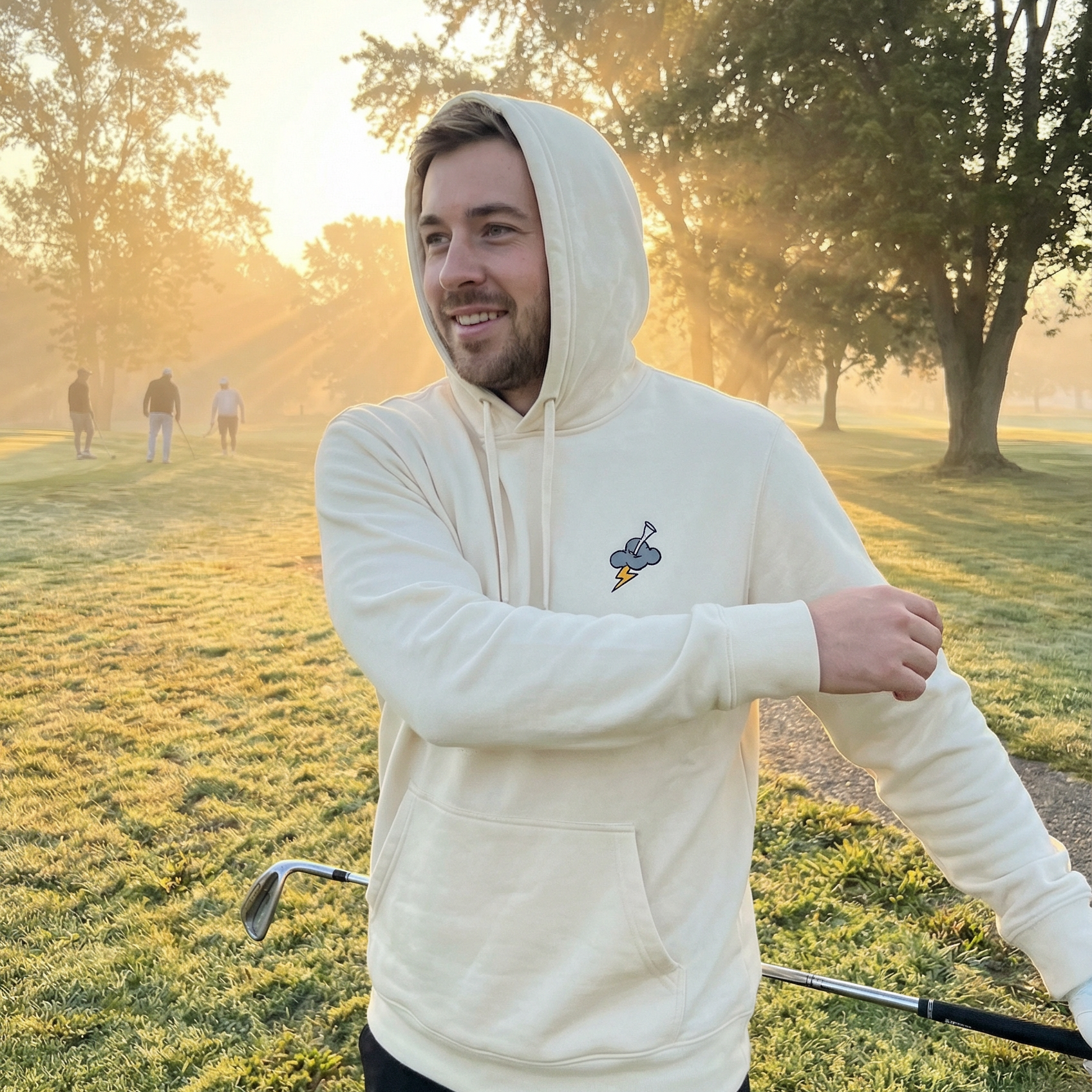 Man in a white hoodie standing on a golf course with trees in the background