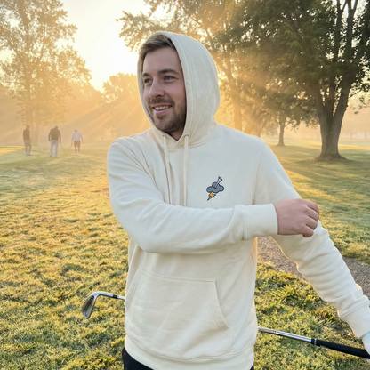 Man in a white hoodie standing on a golf course with trees in the background