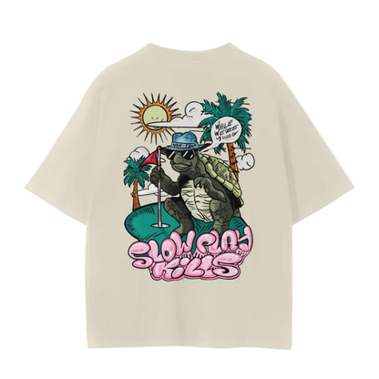A white crew neck t-shirt with a graphic print of a turtle in a sun hat and sunglasses, playing a game of golf, and the text 'SLOW PLAY KILLS' below it.