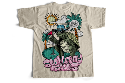 Beige t-shirt with a graphic of a turtle wearing sunglasses and a hat, with palm trees and text on a white background.